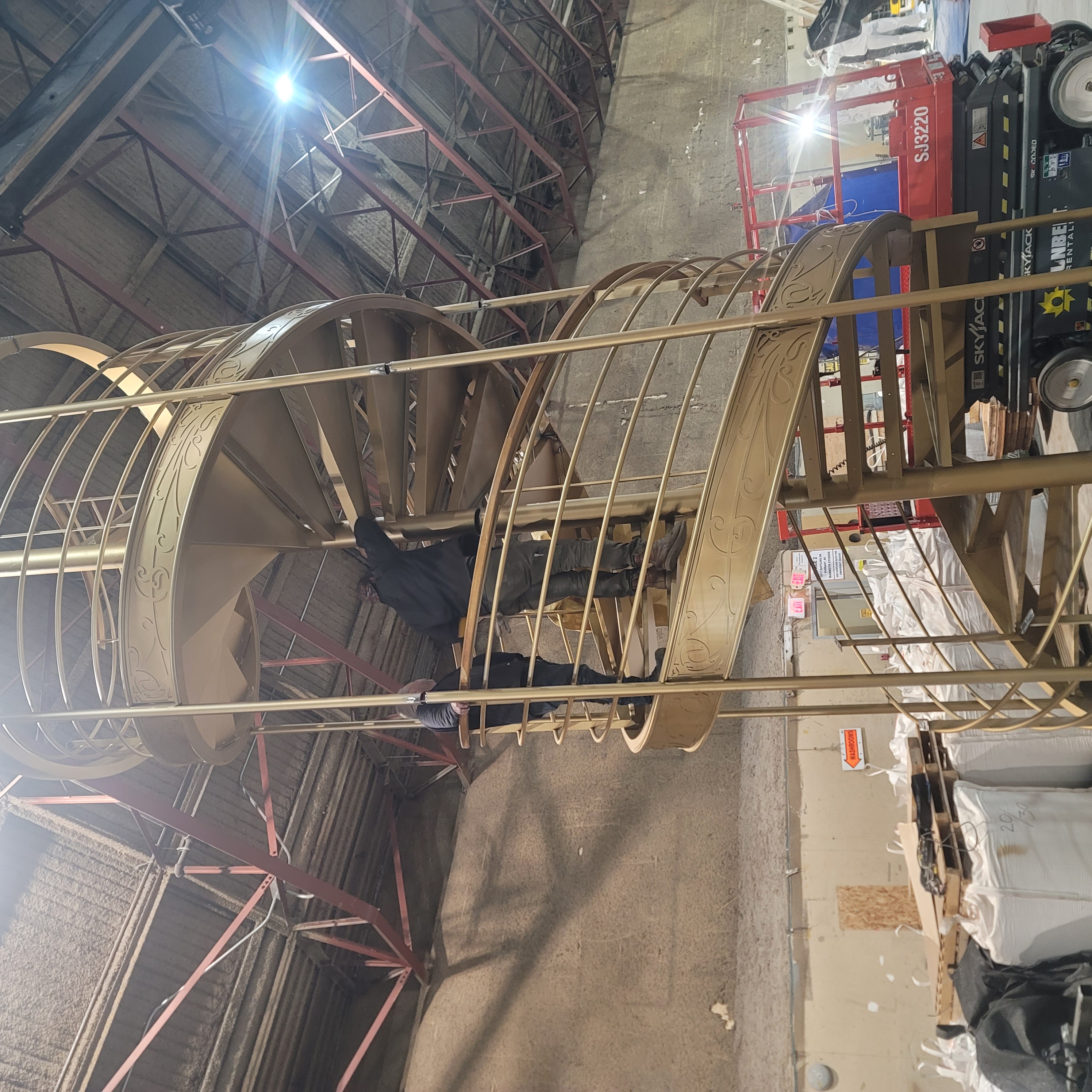 Gold spiral staircase structure being assembled in a fabrication space